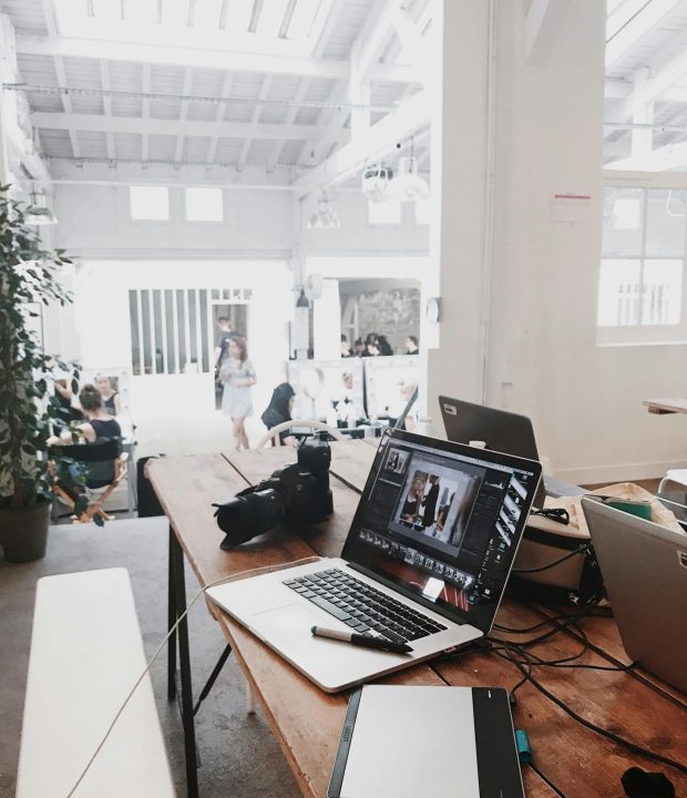 A bright, modern workspace featuring laptops, a camera, and a drawing tablet in an indoor office.